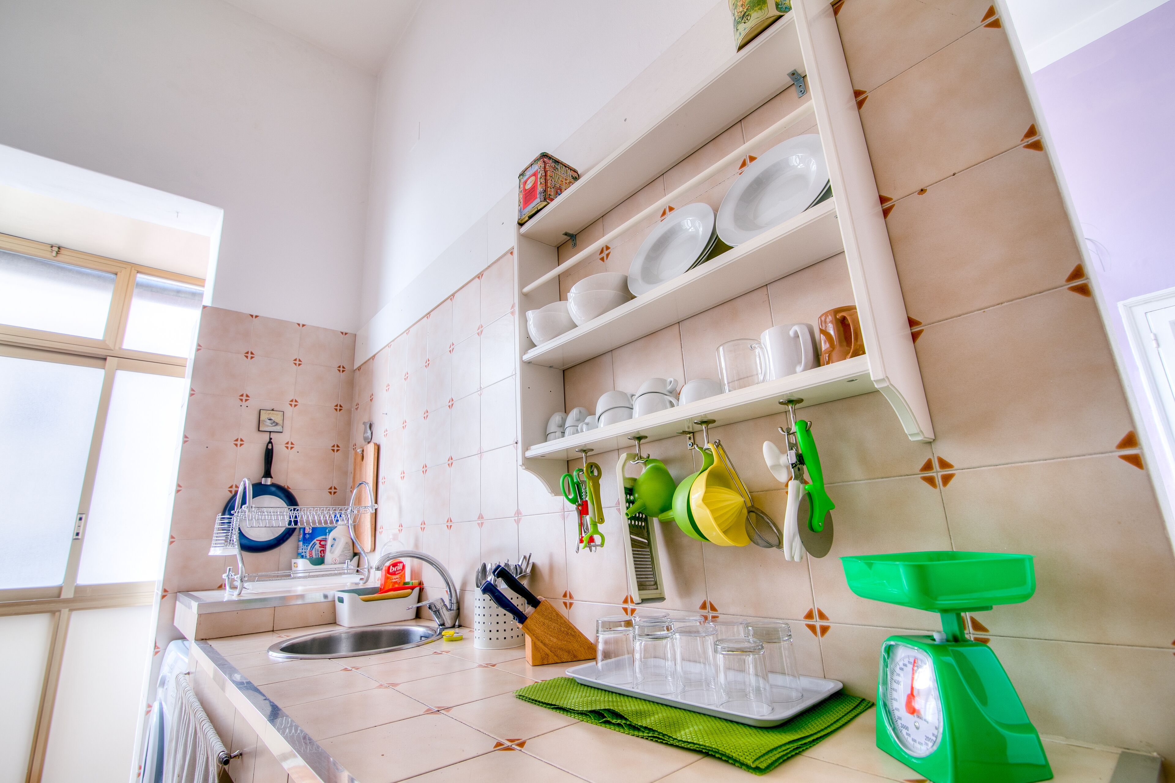 A kitchen with a sink, a dish rack, a green cutting board, and a green scale.