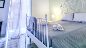 Un dormitorio con cama, mesita de noche, lámpara, ventana con cortinas translúcidas y techo decorativo.