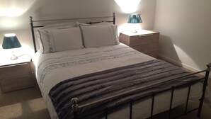 Ein ordentlich bezogenes Bett mit Metallgestell, zwei Nachttische mit Lampen und ein kleiner Holzbeistelltisch.