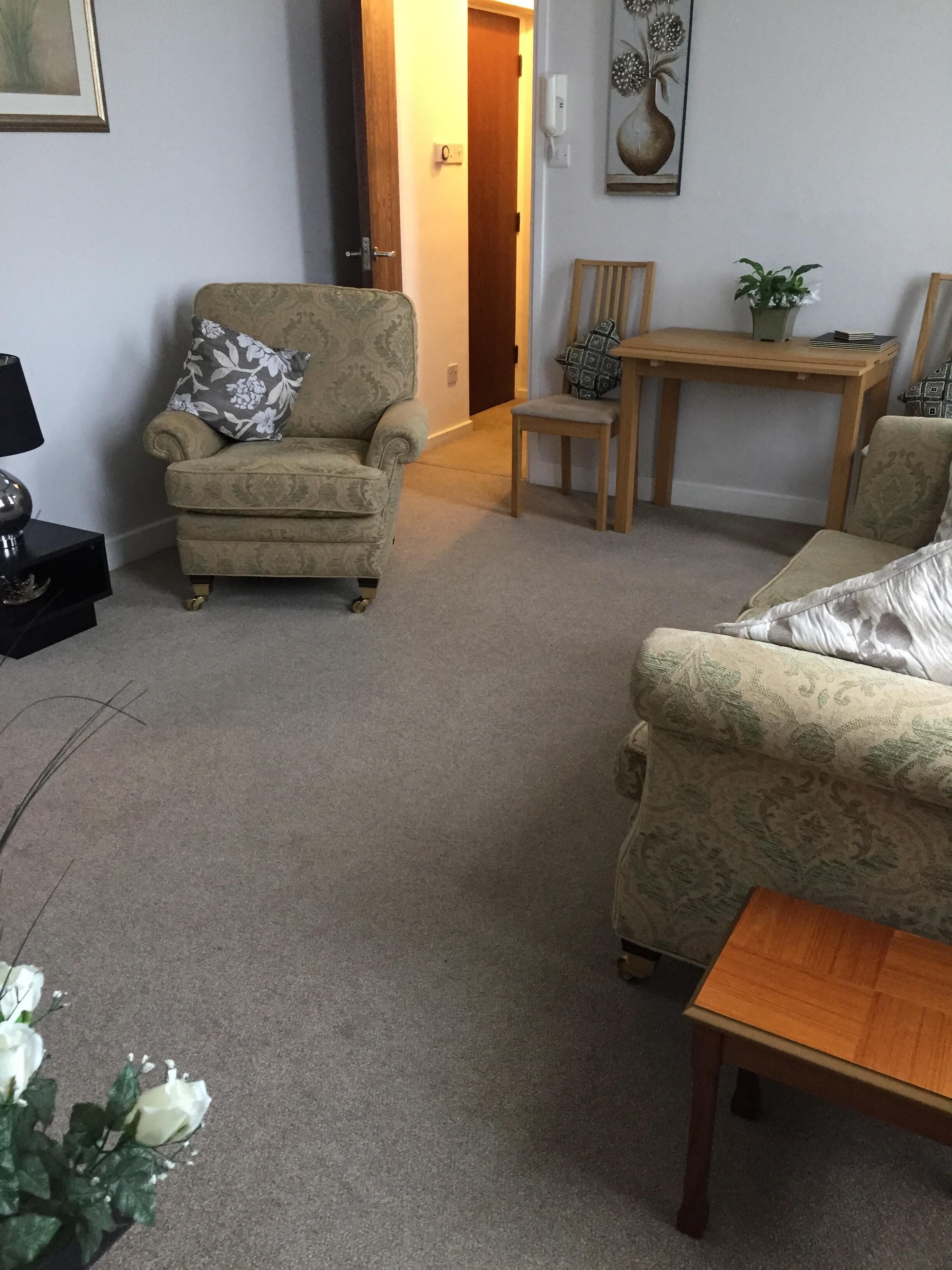 A living room with a beige armchair, a wooden coffee table, and a small table with a plant.