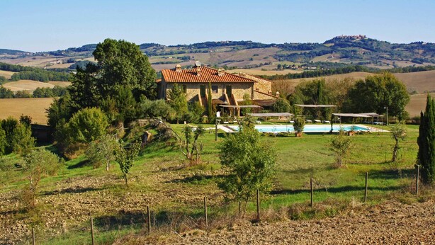 Una villa de piedra con techo de tejas, piscina y vistas a colinas ondulantes al fondo.