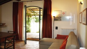 Una sala de estar con un sofá, una mesa de comedor y vista a un área exterior por un vano de puerta.