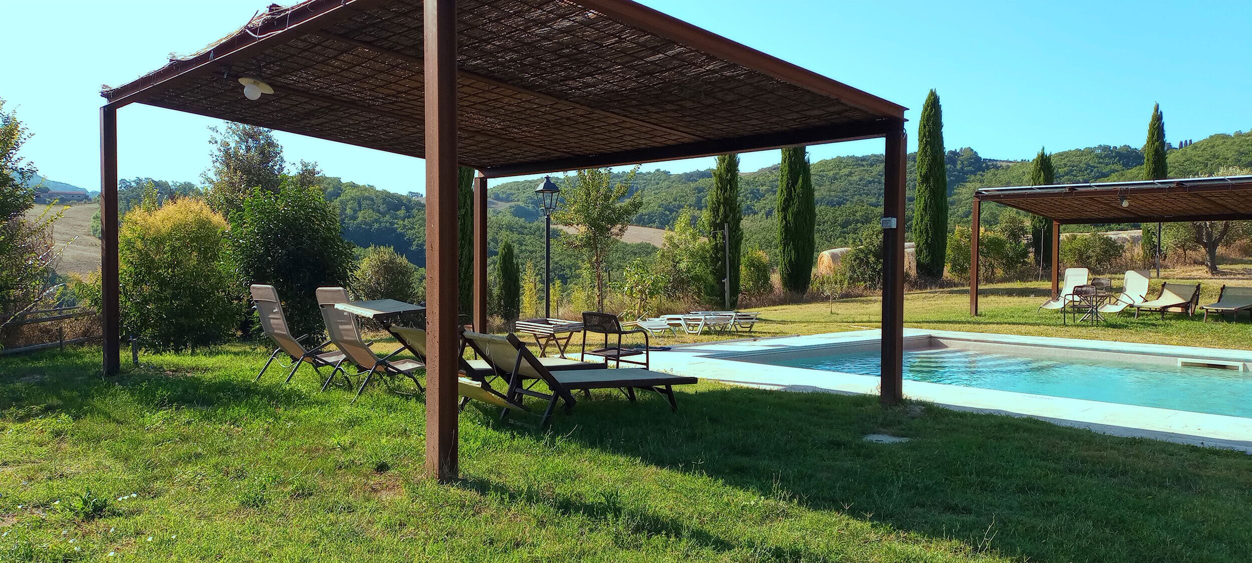 Zona exterior coberta amb piscina, gandules i una pèrgola.