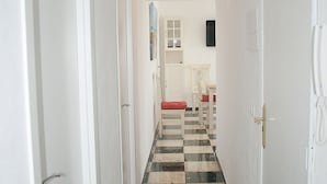 Um corredor com piso xadrez, paredes brancas e portas que dão acesso a quartos.
