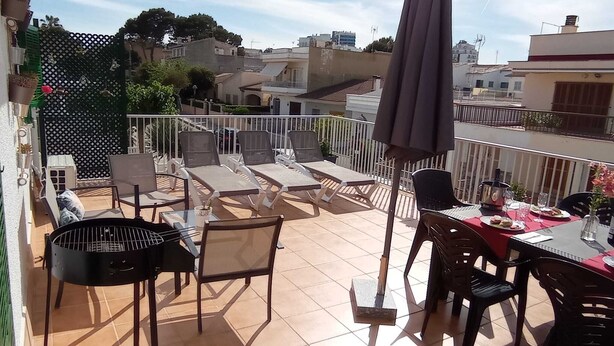 Um terraço com área de estar externa, churrasqueira e mesa posta para refeições.