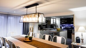 Un espace repas moderne avec une table en bois, des chaises blanches et un luminaire suspendu.