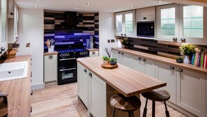 Une cuisine moderne dotée d’un îlot central, d’un four encastré et d’un four à micro-ondes. Les meubles de rangement sont en bois et le mur derrière l’évier est recouvert d’un mélange de carreaux.