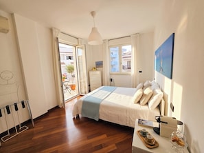 A bedroom with a bed, a desk with a coffee machine, a window with a view, and a door leading to a balcony.
