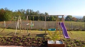 A playground with swings, a slide, and a swing set in a grassy area with trees in the background.