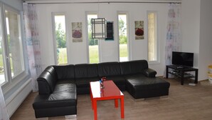 A modern living room with a black leather sectional sofa, a red coffee table, and a flat-screen TV on a stand.