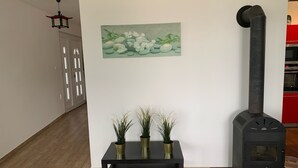 A modern kitchen with a black wood-burning stove, a black table with three potted plants, and a painting of fruits and flowers on the wall.