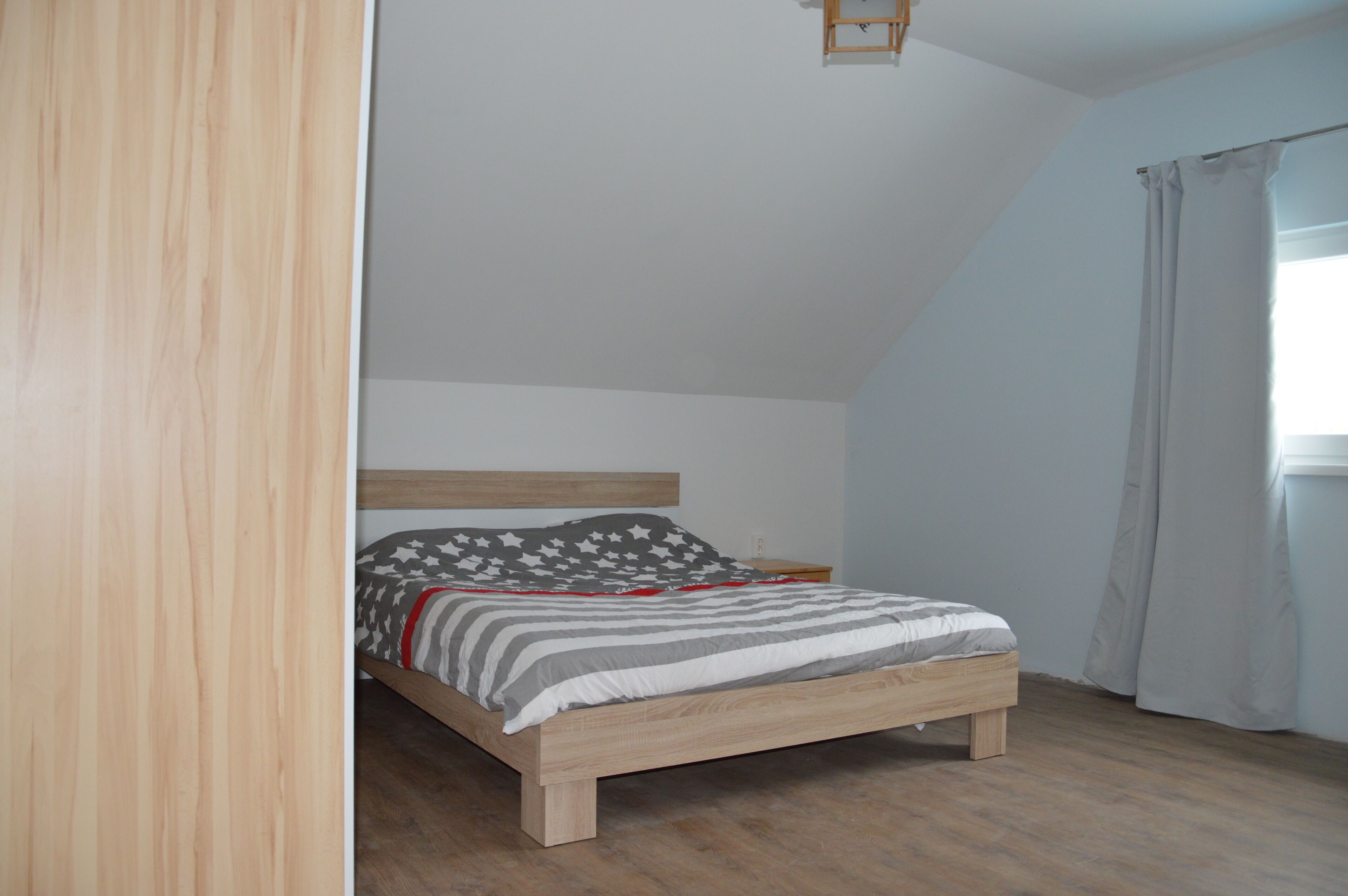 A bedroom with a wooden bed, a headboard, a nightstand, and a window with curtains.