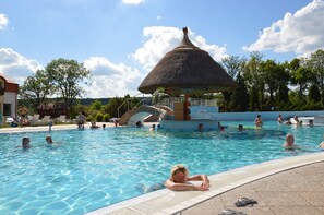 A swimming pool with a thatched-roof structure, surrounded by lounge chairs and trees. - Deluxe villa, large pool, wifi, sauna, jacuzzi, Bedrooms with air conditioning (Nemesbük)