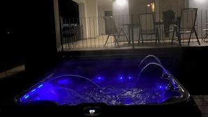 A hot tub with blue lighting, surrounded by a patio area with chairs and a table.