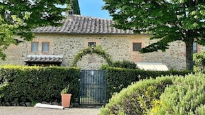Un edificio de piedra con techo de tejas, entrada porticada y setos cuidados.