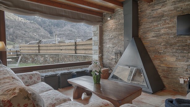 Un salon chaleureux avec une cheminée en pierre, une grande fenêtre donnant sur un paysage montagneux et des sièges confortables.