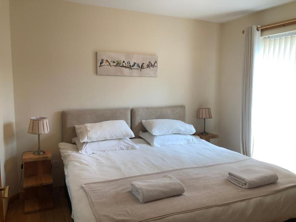 A hotel room with a large bed, two bedside tables, a wall-mounted artwork, and a window with curtains.