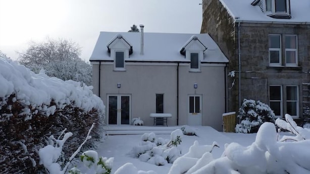 Una casa de dos pisos con tejado nevado y un pequeño garaje adosado.