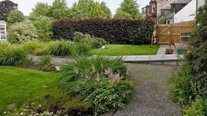 Un jardín con un sendero de grava, diversas plantas y una cerca de madera.