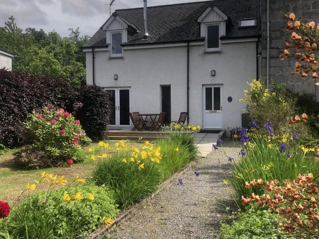 Une maison à deux étages avec un porche à l’avant, un jardin agrémenté de différentes fleurs et un chemin menant à l’entrée.