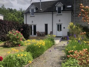 Een woonhuis met twee verdiepingen, een voortuin met diverse bloemen en een pad naar de ingang.