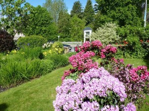 Een verzorgde tuin met diverse bloeiende planten en een wit gebouw op de achtergrond.