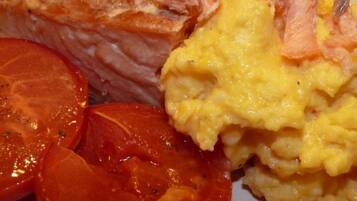 Un plato con salmón, huevos revueltos y rodajas de tomate.