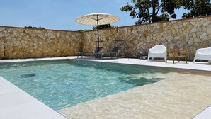 Una piscina amb parets de pedra, gandules blanques i un parasol.