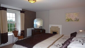 Un dormitorio con cama, una silla, una chimenea y un cuadro en la pared.