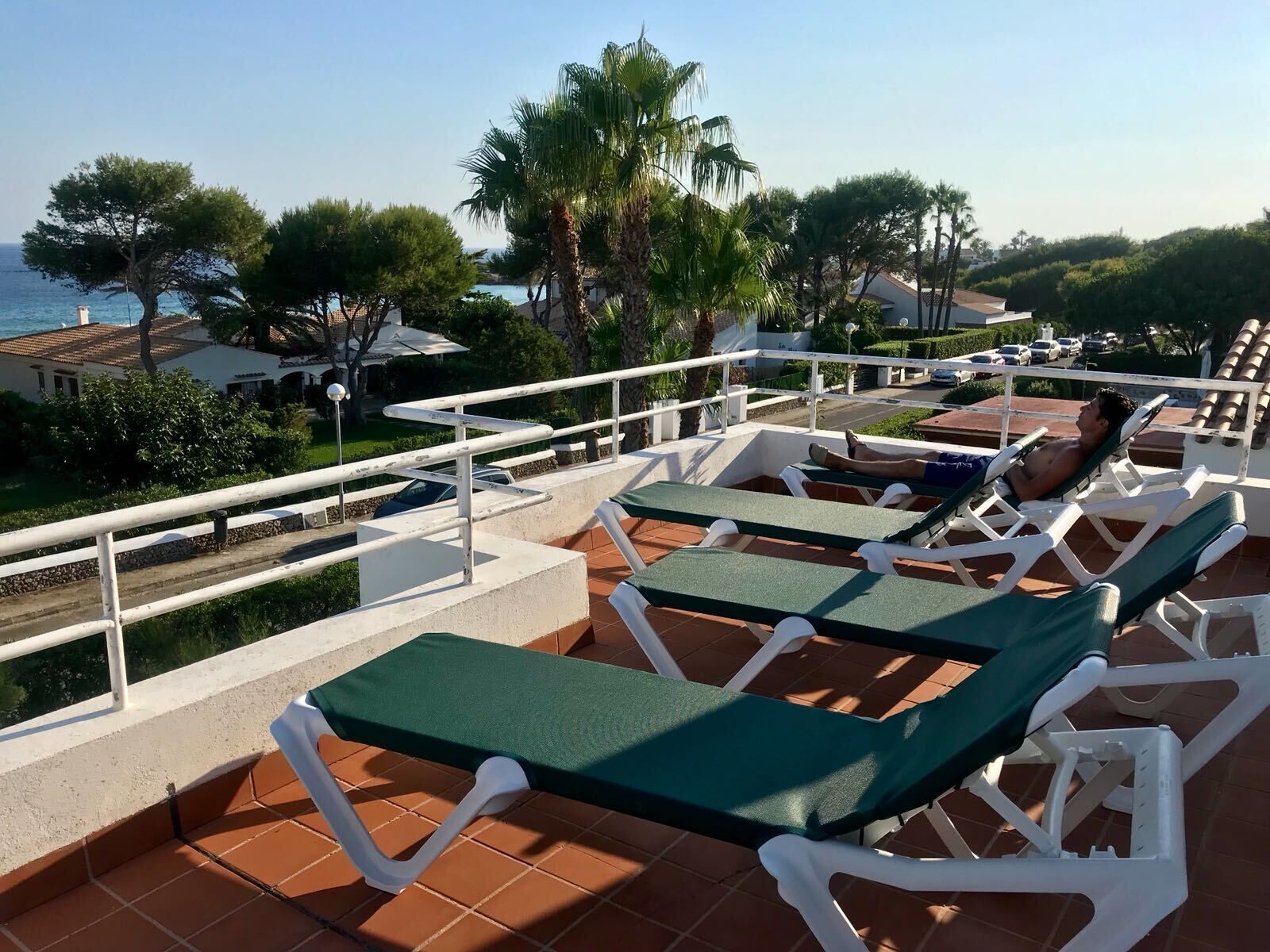 Eine Terrasse mit Liegestühlen mit Blick auf einen Strand und Palmen.