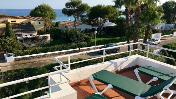 A terrace with two green lounge chairs, a white railing, and a view of the sea and houses.