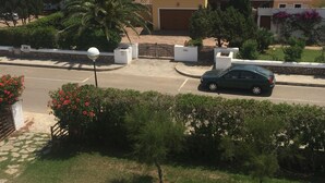 A residential area with a house featuring a tiled roof, a garage, and a well-maintained garden with palm trees and red flowers.