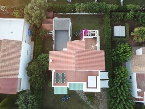 Ein Luftbild einer Wohngegend mit einem Haus, das ein Ziegeldach, eine Terrasse mit Pool und einen Garten mit verschiedenen Pflanzen und einem kleinen Baum zeigt.