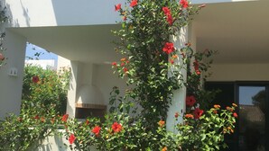 A white building with a balcony, a staircase, and a garden with red flowers.
