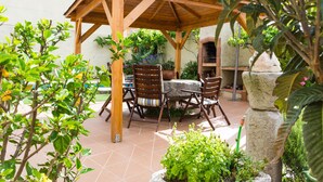 A wooden pergola with a table and chairs, surrounded by greenery and a stone sculpture. - Spacious and bright apartment on the Costa Brava, landscape of the painter S. Dalí (Castelló d'Empúries)
