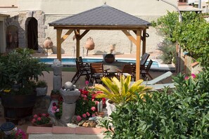 Un patio techado con mobiliario exterior, una piscina y diversas plantas en macetas.