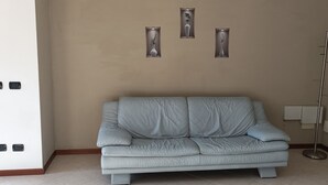 A light gray sofa in a room with beige walls, a floor lamp, and three wall-mounted light fixtures. - Gemma - apartment holiday home (Desenzano del Garda)