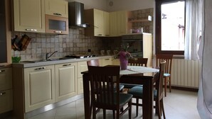 A kitchen with light-colored cabinets, a stove, and a dining area with wooden chairs. - Gemma - apartment holiday home (Desenzano del Garda)