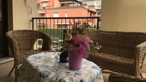 A balcony with wicker furniture, a table with a floral tablecloth, and a vase with flowers. - Gemma - apartment holiday home (Desenzano del Garda)