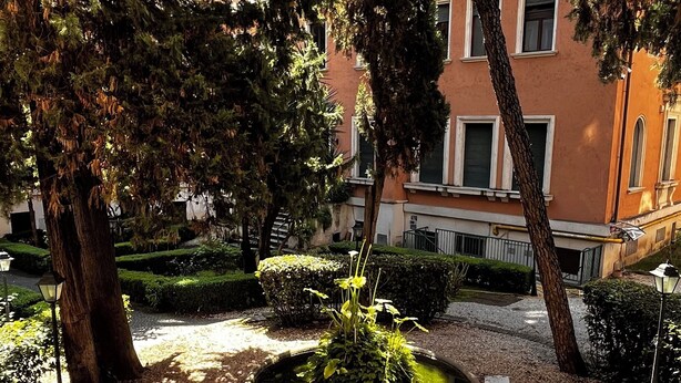 A courtyard with a central fountain, surrounded by trees and a building with multiple windows.