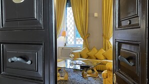 A room with a dark wooden door, a yellow sofa, a glass coffee table, and a patterned rug.