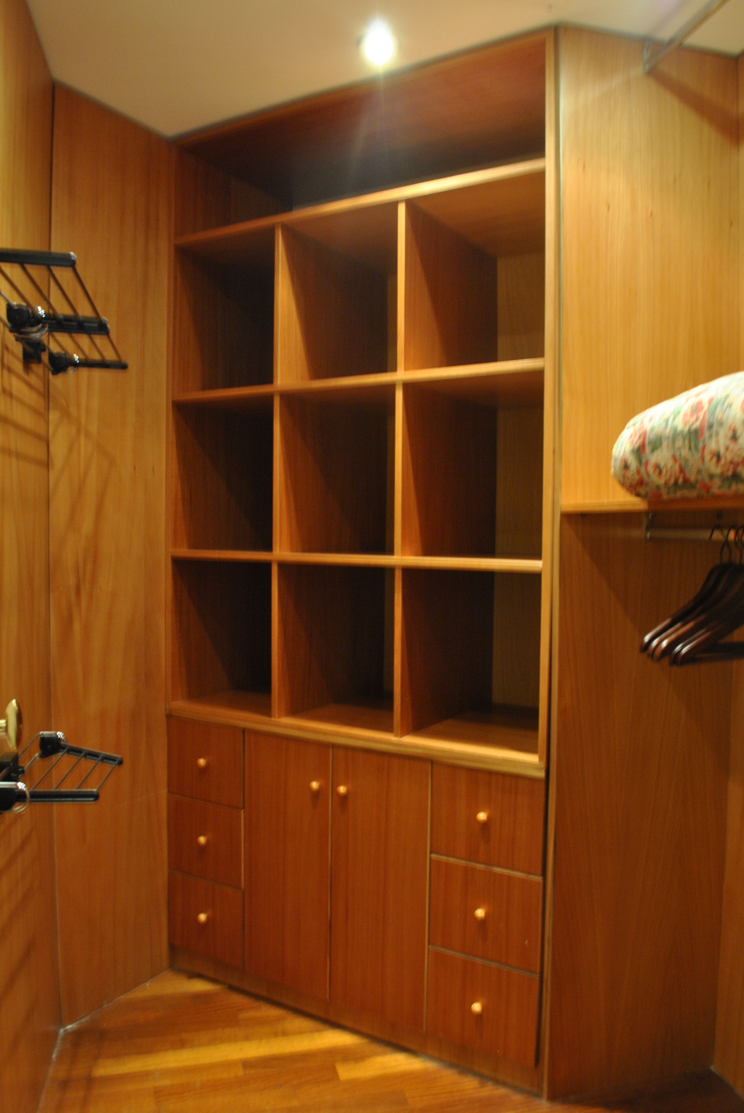 Une armoire en bois dotée de nombreuses étagères et de tiroirs, d’une tringle pour suspendre les vêtements et d’un objet décoratif à motifs floraux placé sur le dessus.