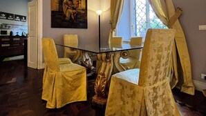 A room with a dining table and chairs, a painting on the wall, and a window with curtains.