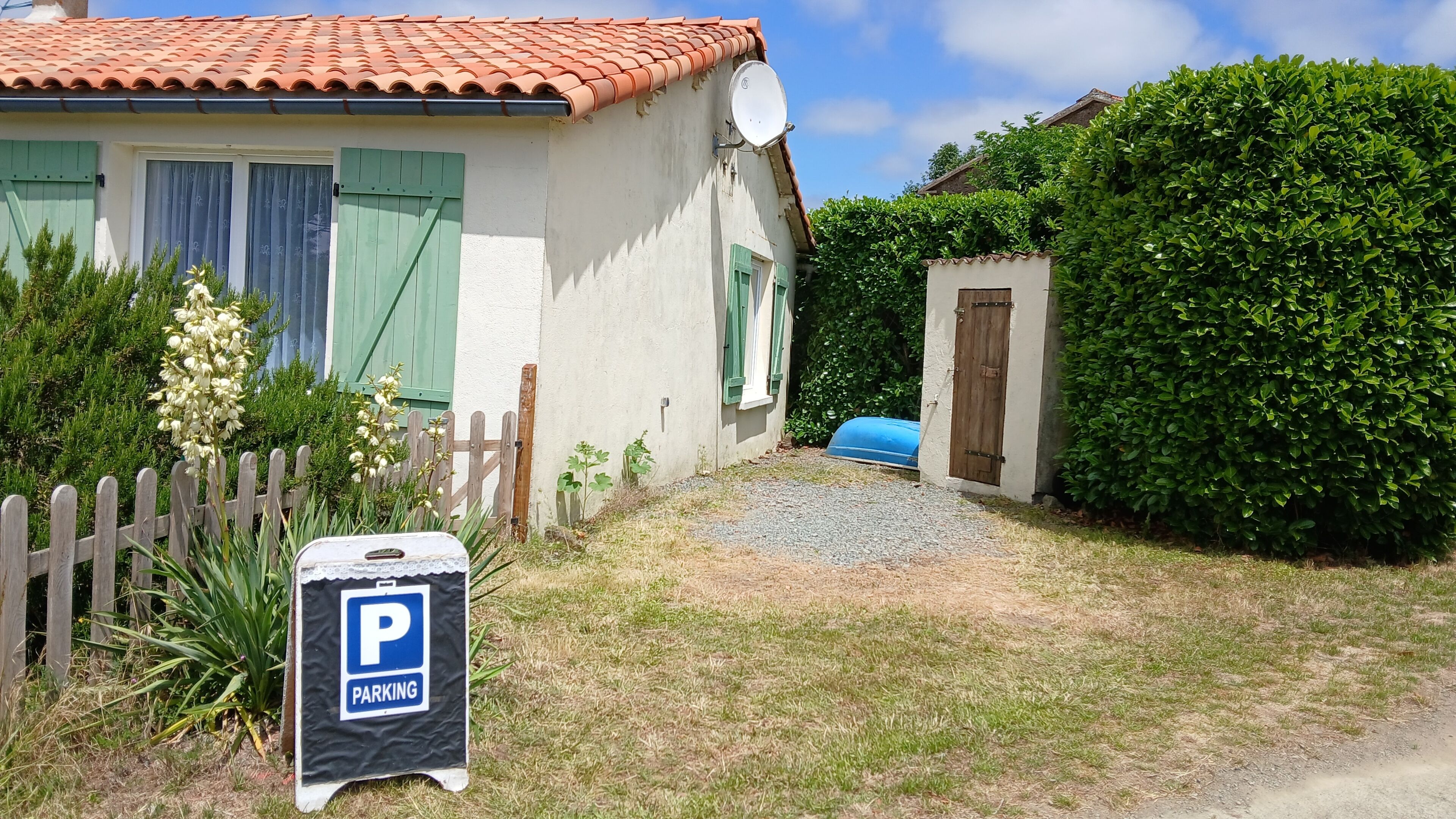 Une maison avec un toit en tuiles, une antenne parabolique, une clôture en bois et un panneau indiquant un espace de stationnement.