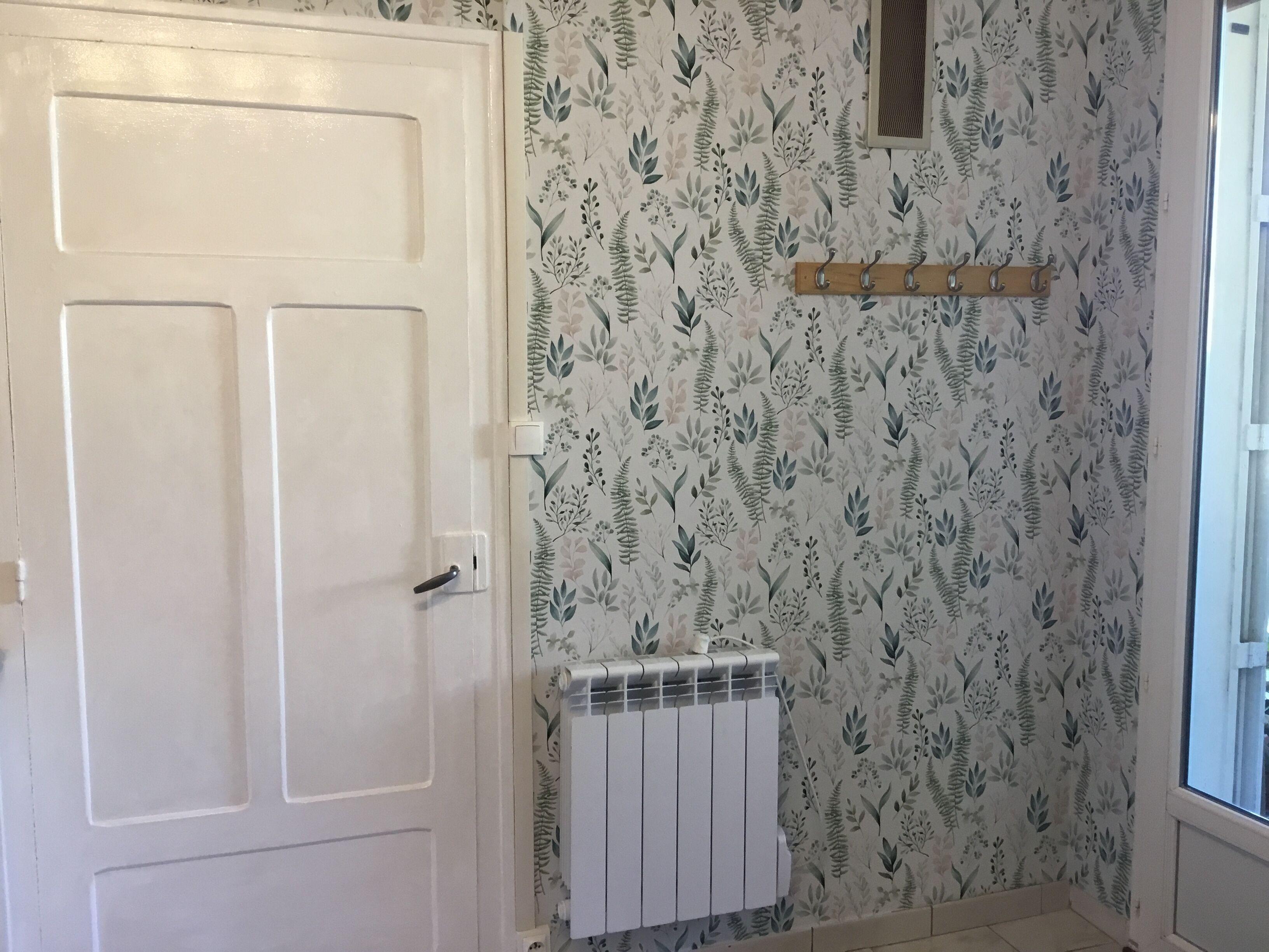 A bathroom with a white door, a radiator, and a wall with a leafy pattern.