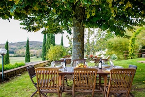 An outdoor dining area with a wooden table and chairs, surrounded by greenery and trees.