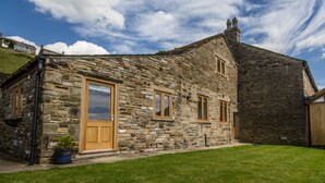 A stone building with a wooden door and windows, a grassy yard, and a clear sky. - High Peak converted barn with private garden and stunning views  (HIGH PEAK)