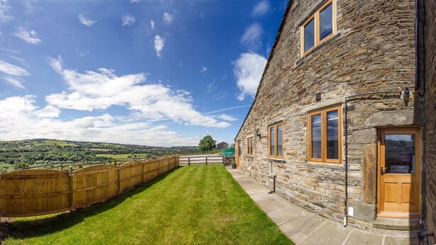 A stone building with a wooden door and windows, a grassy lawn, and a view of the countryside. - High Peak converted barn with private garden and stunning views  (HIGH PEAK)