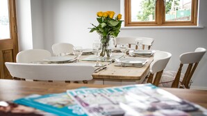 A dining table set for six with white chairs, a vase of yellow roses, and a magazine on the table. - High Peak converted barn with private garden and stunning views  (HIGH PEAK)