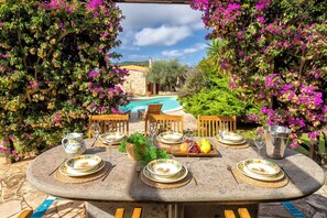 An outdoor dining area with a pool view, surrounded by flowering plants.